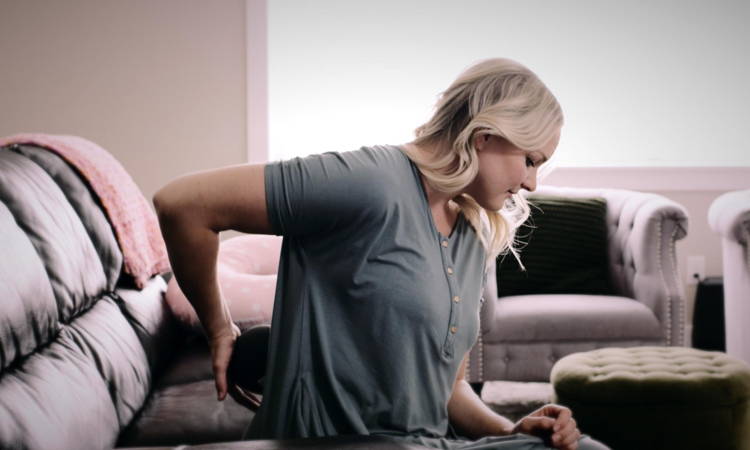 Blonde woman using Meteor massage ball on her lower back while sitting on the couch.