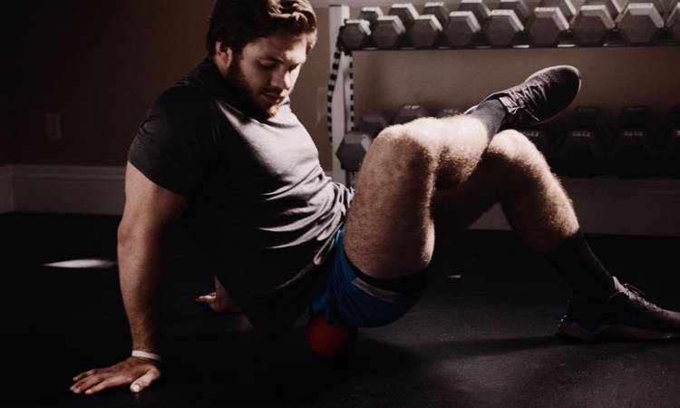 Man using Meteor massage ball on lower back after a workout at the gym.