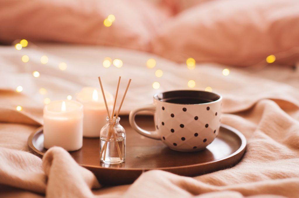 A tray holding chamomile tea, candles, and an oil diffuser on a cozy bed at bedtime