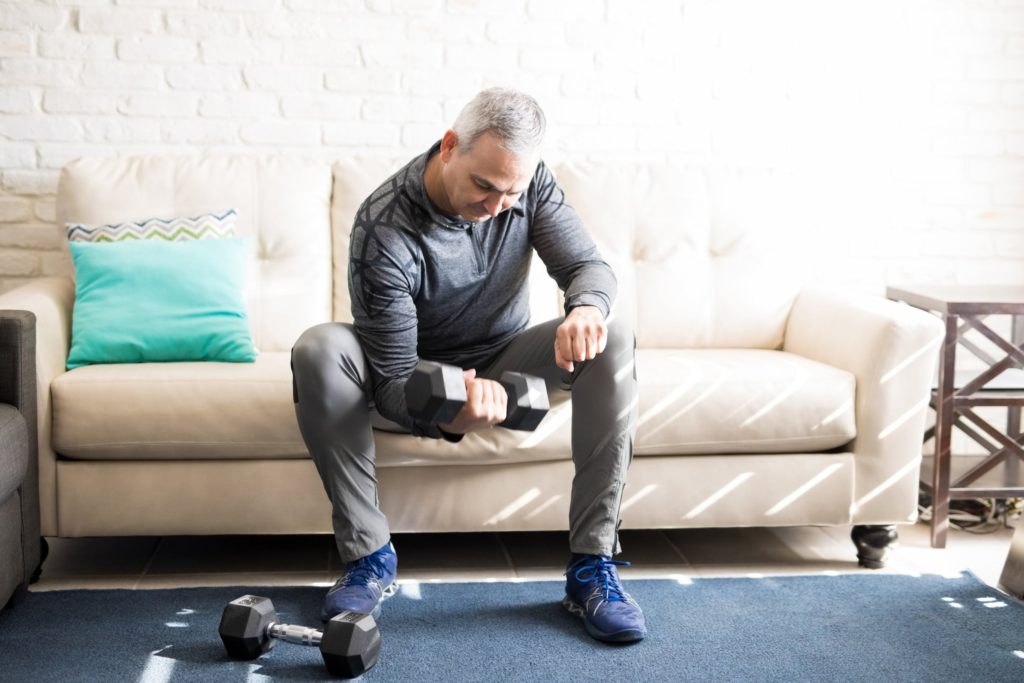 man using a dumbbell at home on his couch