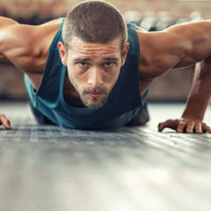 Fit male wearing a tank top and performing push-ups at the gym