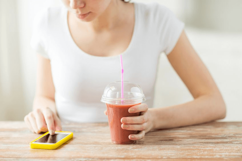 A woman using a vegan recipe app while drinking a vegan smoothie